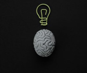 Gray brain with light bulb symbol on black background representing intelligence and creativity.